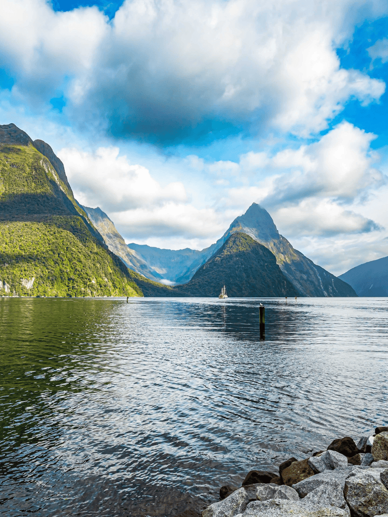 Serene fjord landscape with mountains, water, and sailboat, showcasing New Zealand's natural beauty.