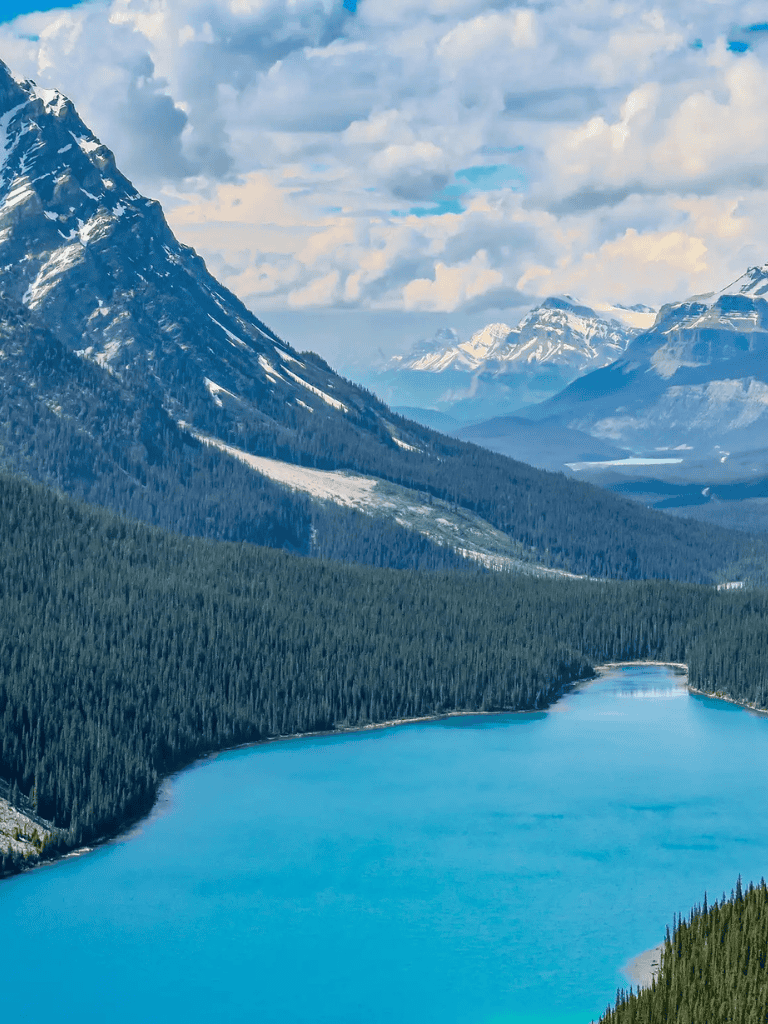 Serene mountain lake with snow-capped peaks and lush evergreen forests in the background.