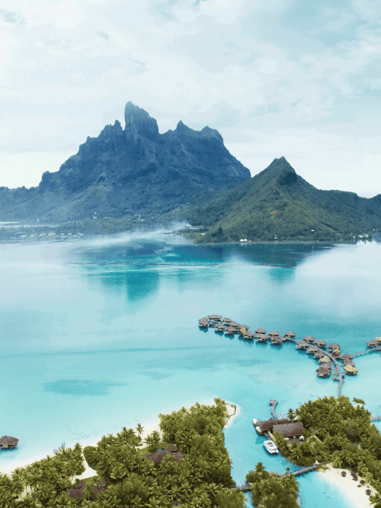 Breathtaking tropical island with overwater bungalows and lush greenery near towering mountains.