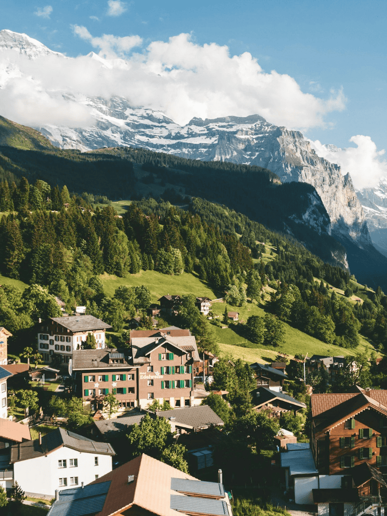 Mountain village in the Swiss Alps with lush green trees and snow-capped peaks.