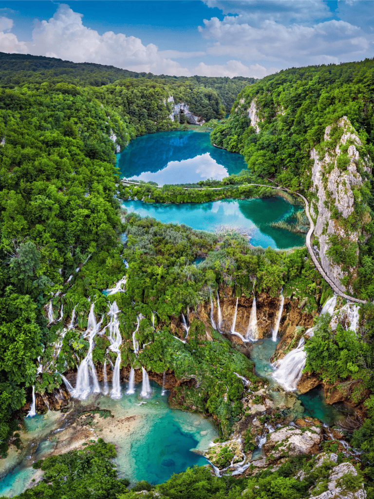 Vibrant waterfall cascading into turquoise lakes surrounded by lush green forest and scenic mountain views.
