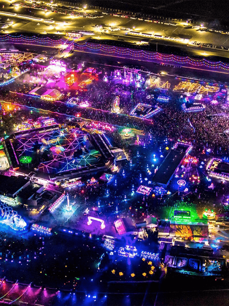 Brightly lit carnival at night with colorful rides and attractions, vibrant neon lights, and large crowds enjoying the festivities.