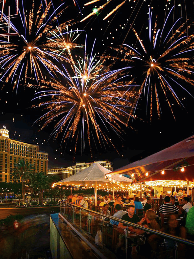 Spectacular fireworks display over a lively outdoor restaurant at night in Las Vegas.