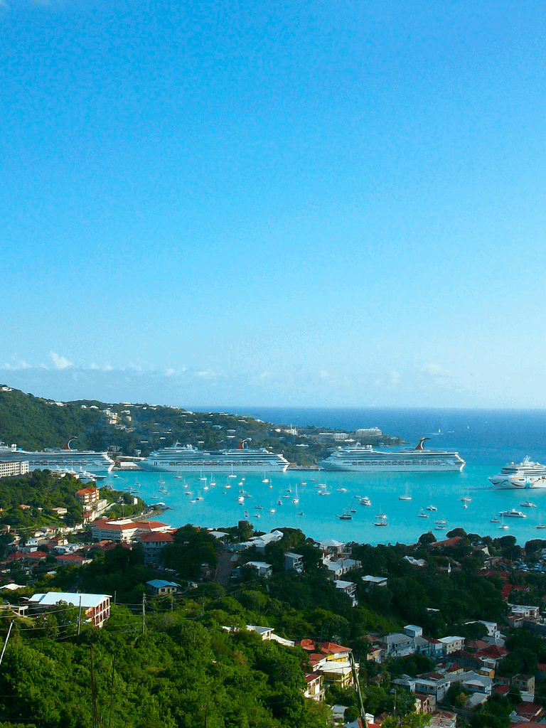 Cruise ships at harbor in tropical island destination with lush greenery and boats in turquoise water.