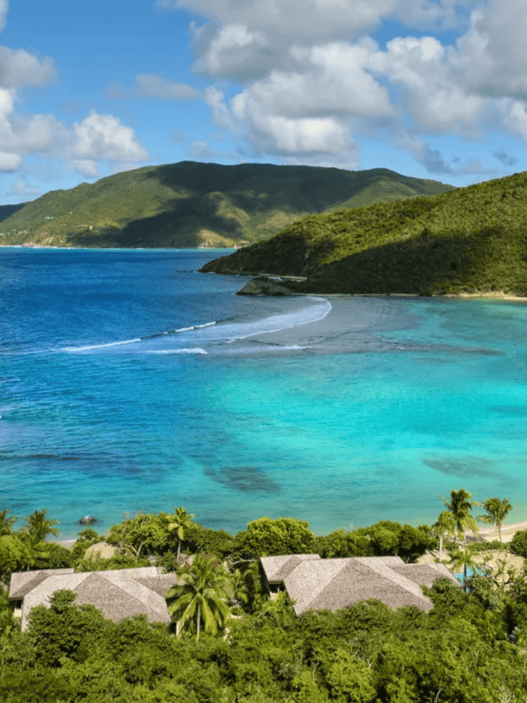 Tropical beach coastal landscape with lush green hills and clear blue water.