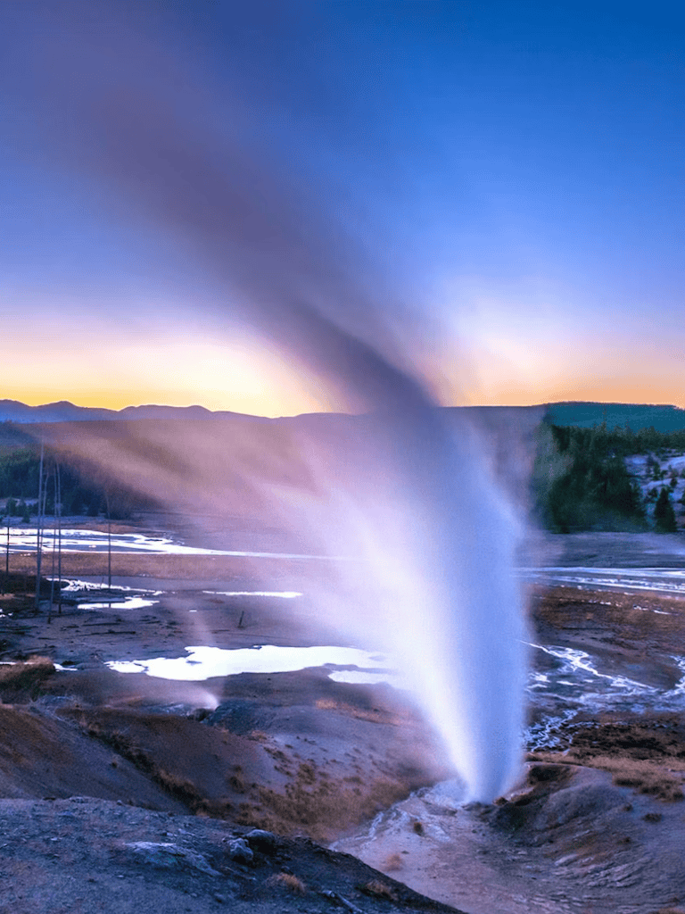 Spouting geyser erupting in Yellowstone National Park during sunset.