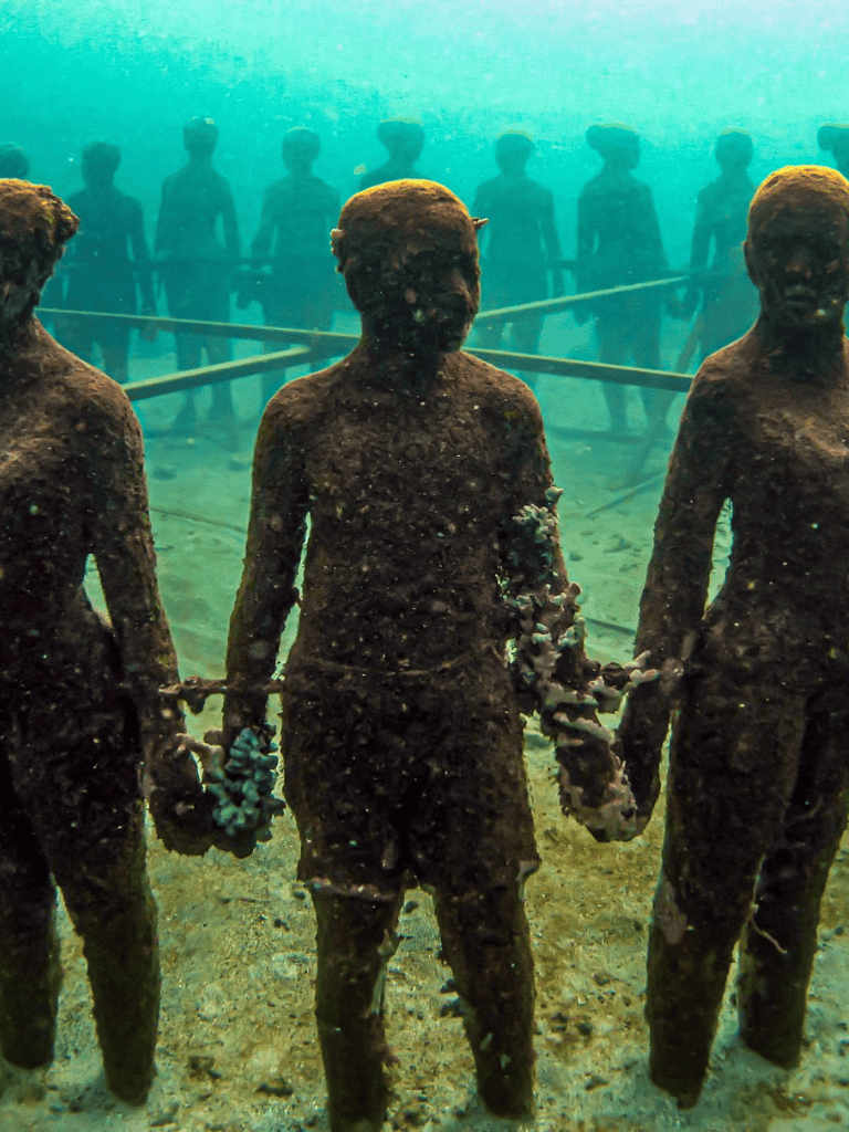 Children holding hands underwater sculpture, exploring submerged art at Quest For Directions, an underwater museum exhibit.
