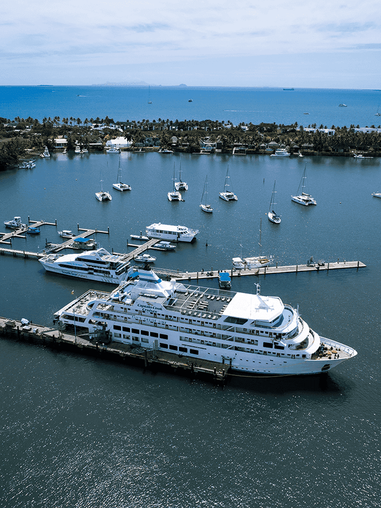 Luxury yacht docked at marina with sailboats and ocean in background, scenic coastal views.