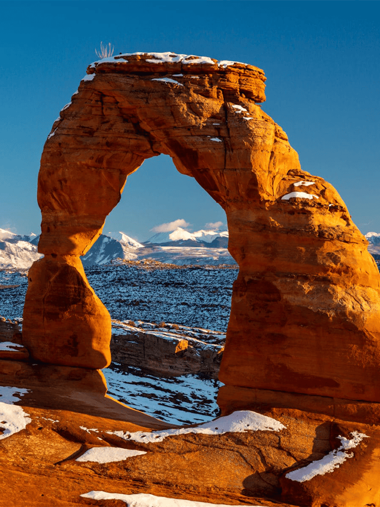 Majestic desert rock formation with snow-capped mountains in the background, showcasing natural beauty and outdoor adventure.