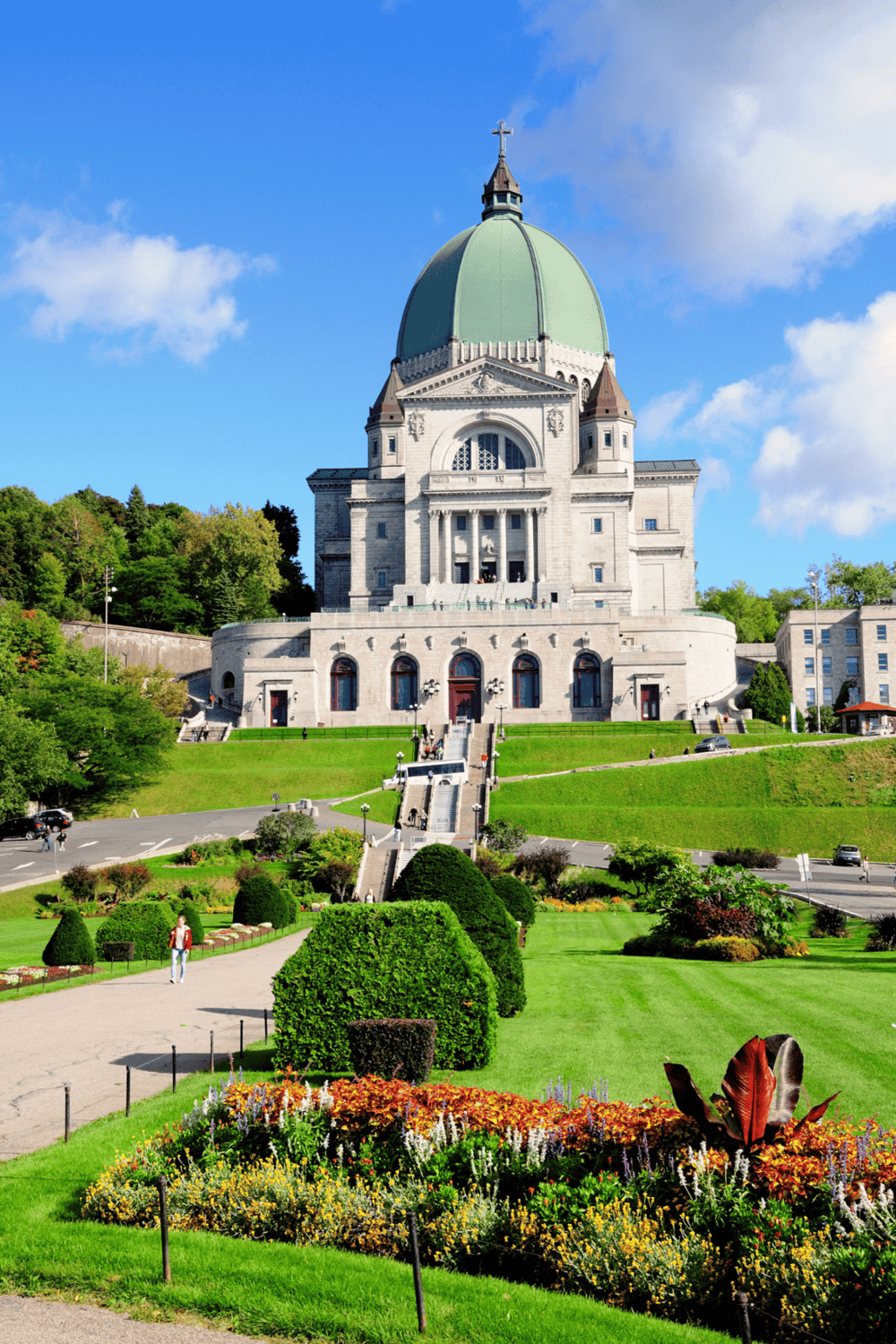 Majestic church with green dome atop hill, surrounded by lush gardens and vibrant flowers.