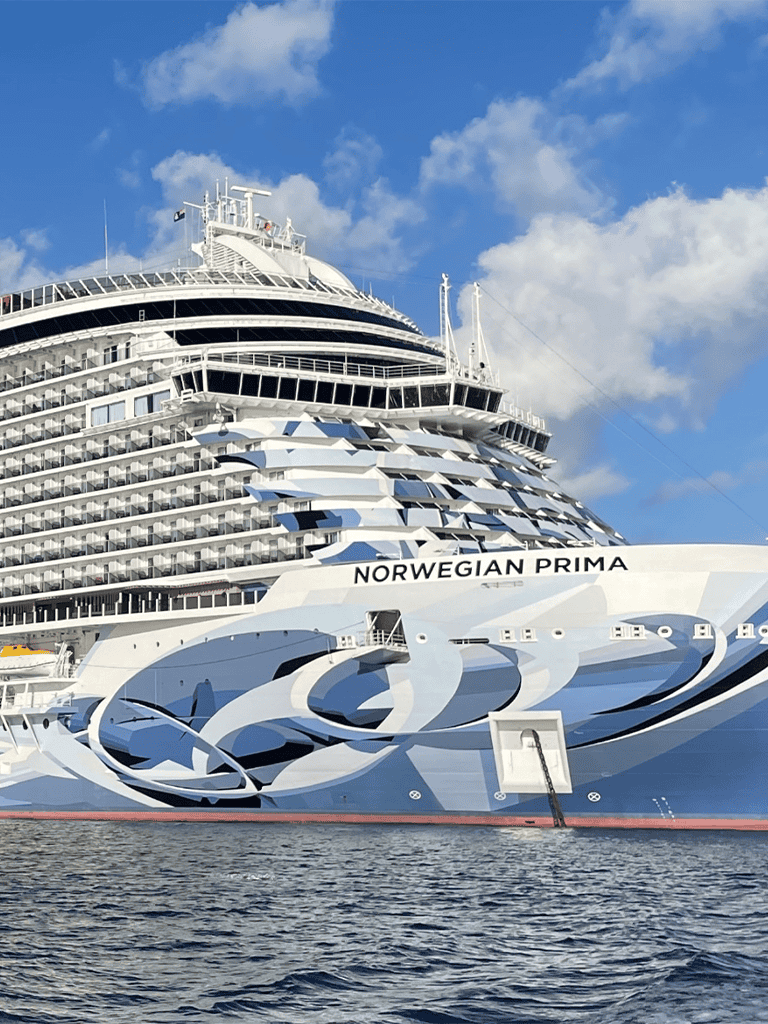 Luxury cruise ship Norwegian Prima sailing on the ocean under blue sky.