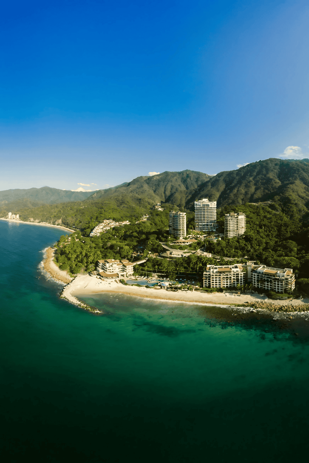 Luxury beachfront resort with lush green mountains and clear ocean waters in Cabo San Lucas.
