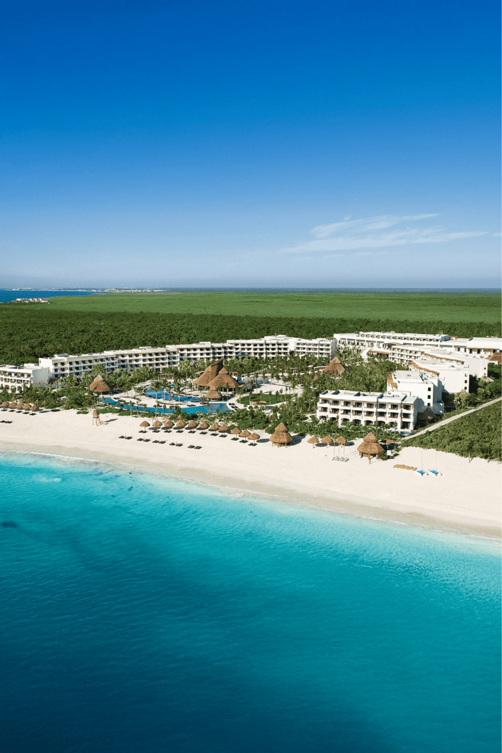 Luxurious beachfront resort with pools, palm trees, and white sandy beach on turquoise ocean.