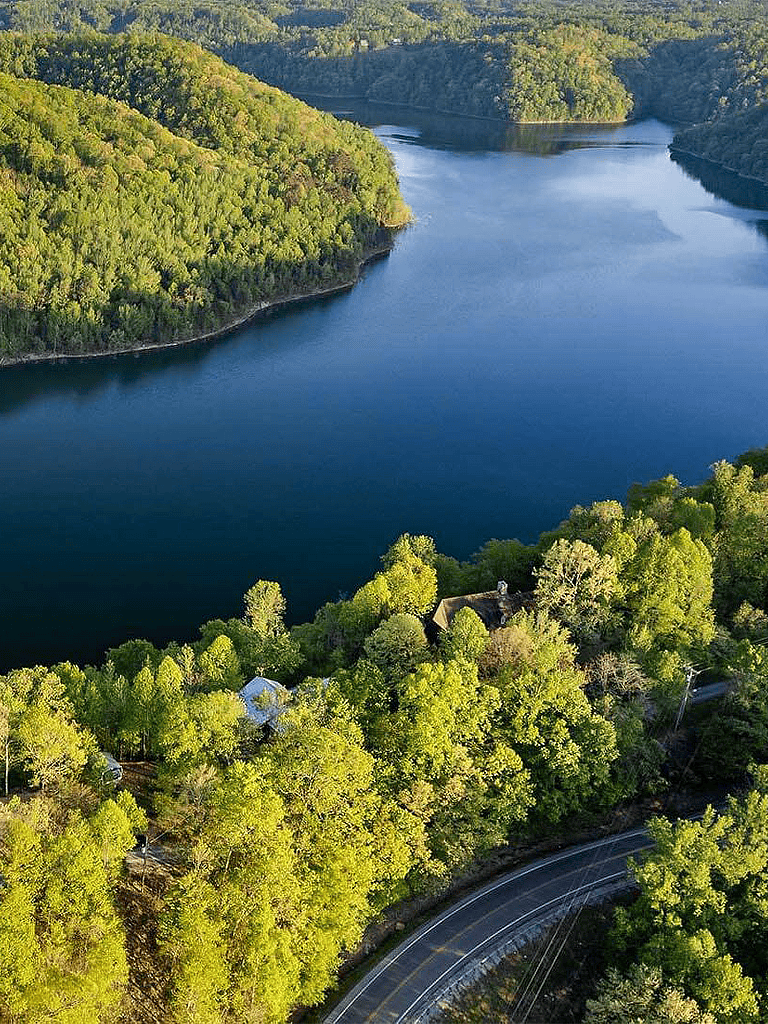 Serene lake surrounded by lush green forests and winding road in a scenic wilderness area.