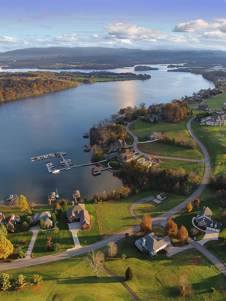 Serene lakeside neighborhood with houses, boat docks, and scenic water views during autumn.