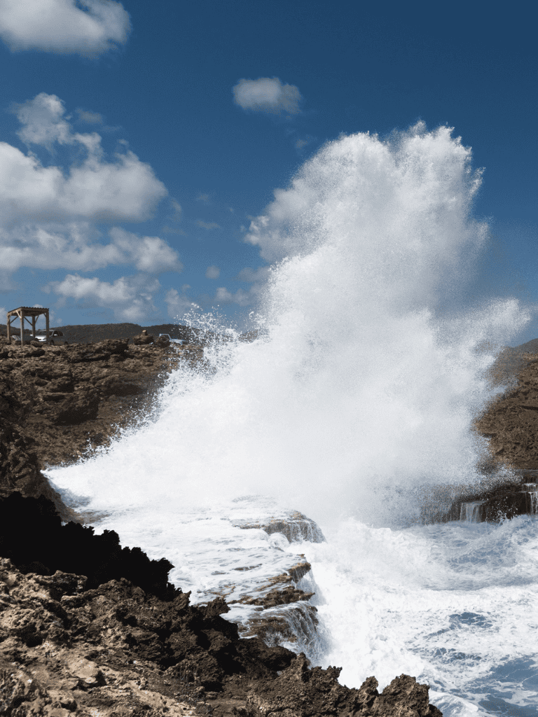 Crashing ocean waves on rocky coast in clear blue sky.