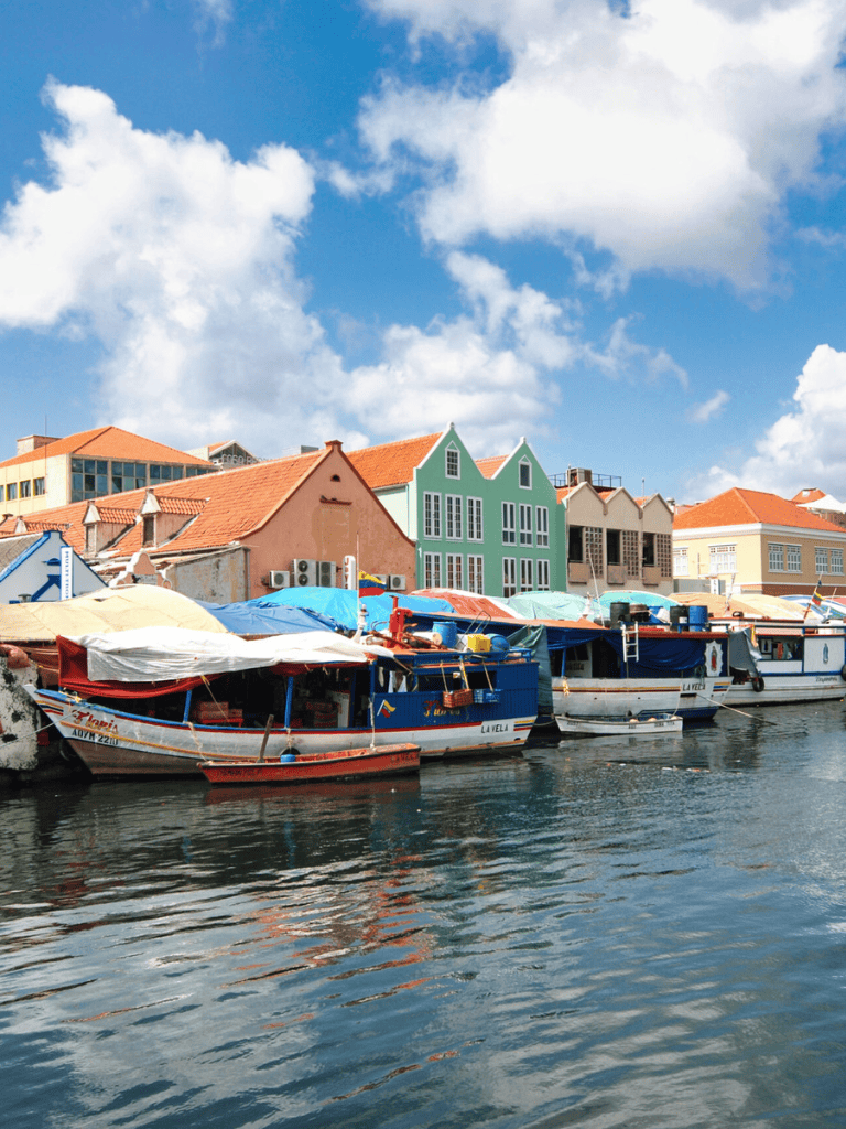 Colorful boats docked along a vibrant waterfront with pastel buildings under a partly cloudy sky in a scenic harbor.