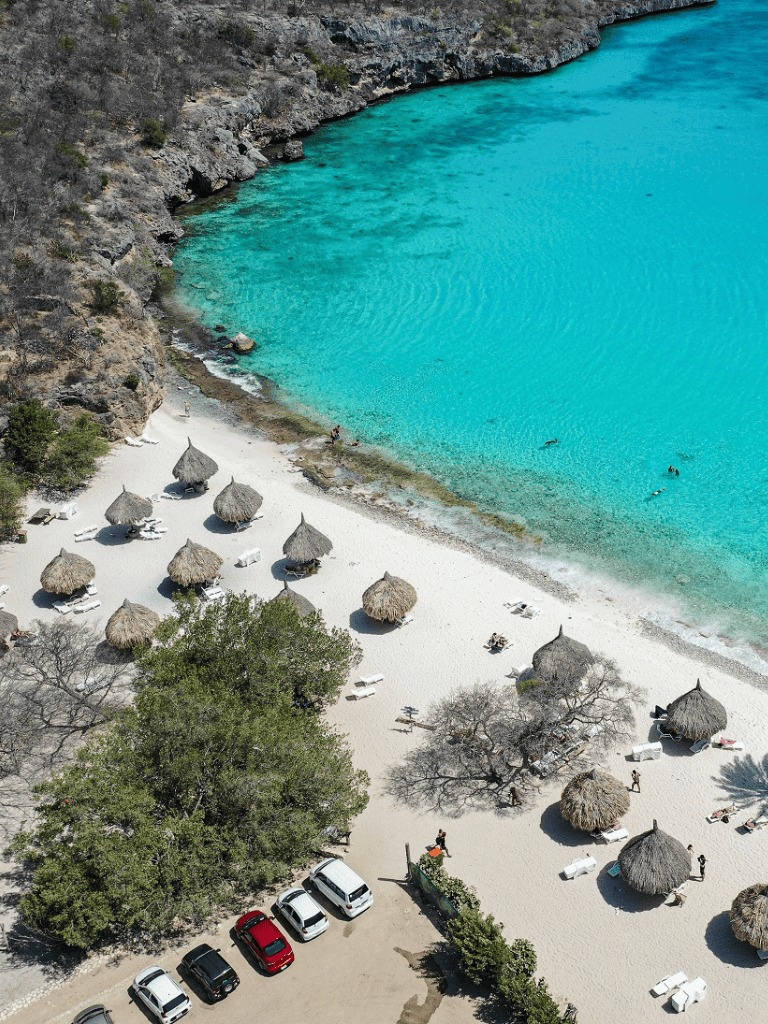 Turquoise beach with thatched umbrellas and lush greenery, perfect for relaxing seaside holidays.