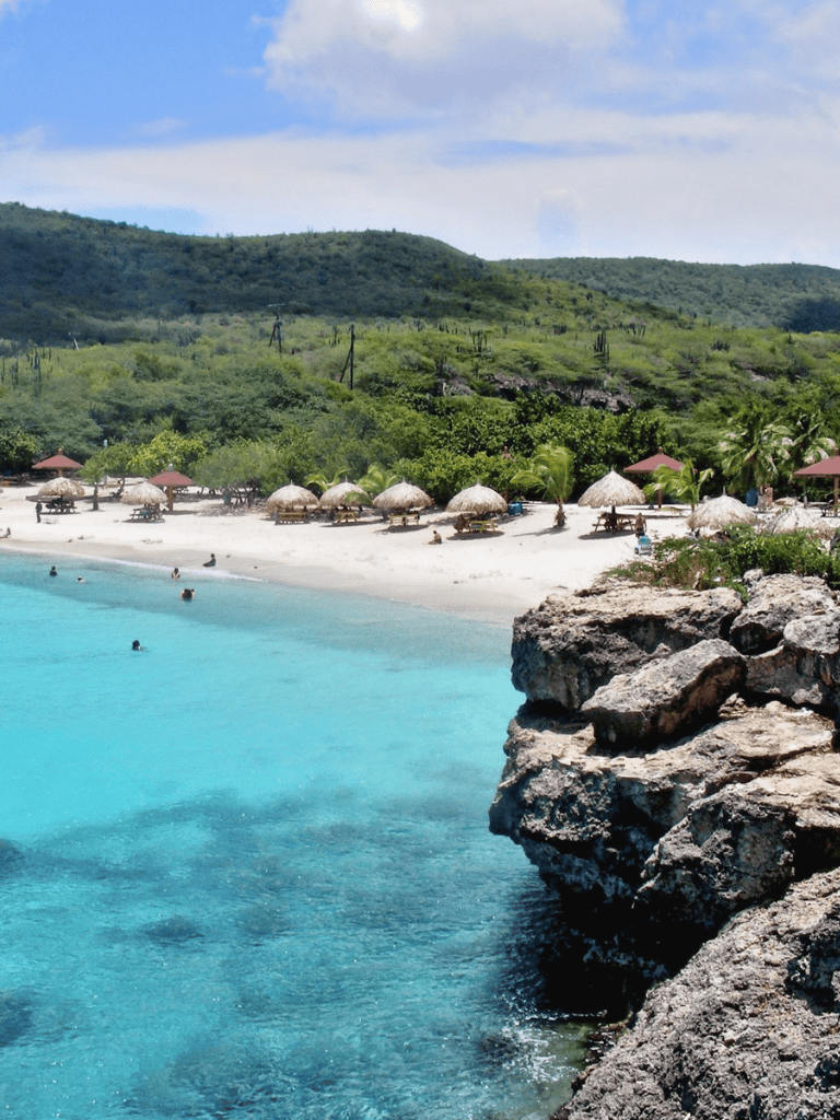 Stunning tropical beach with clear blue water, white sand, and lush green hills in the background.