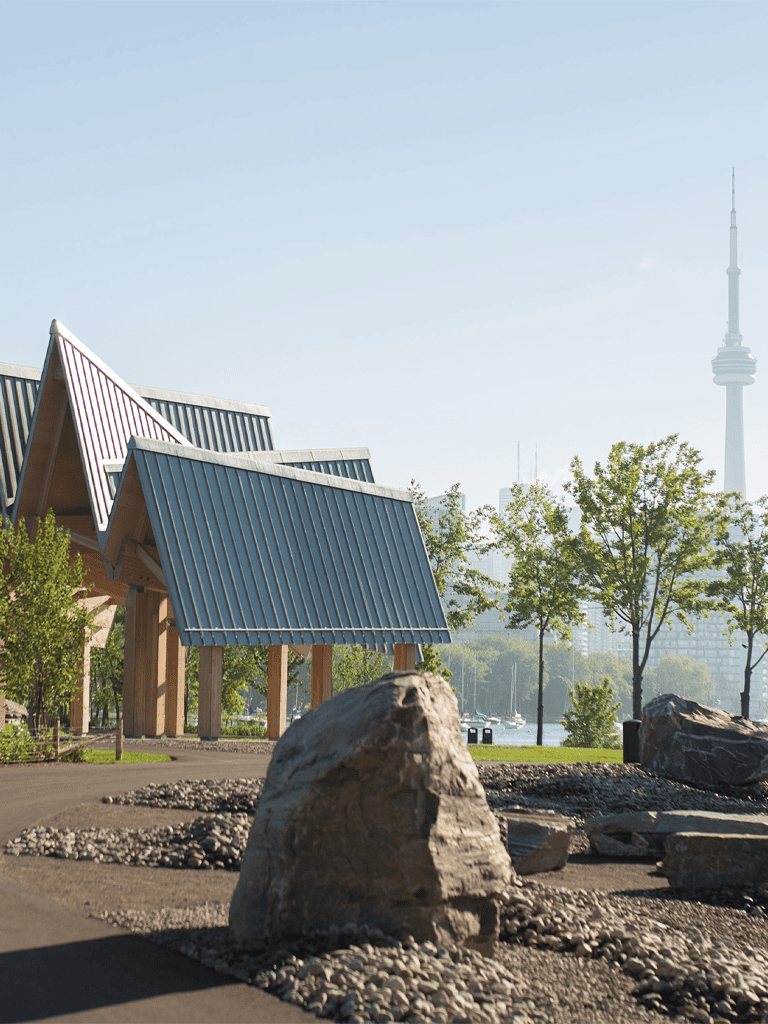 Modern park with unique wooden structures and Toronto skyline in background.