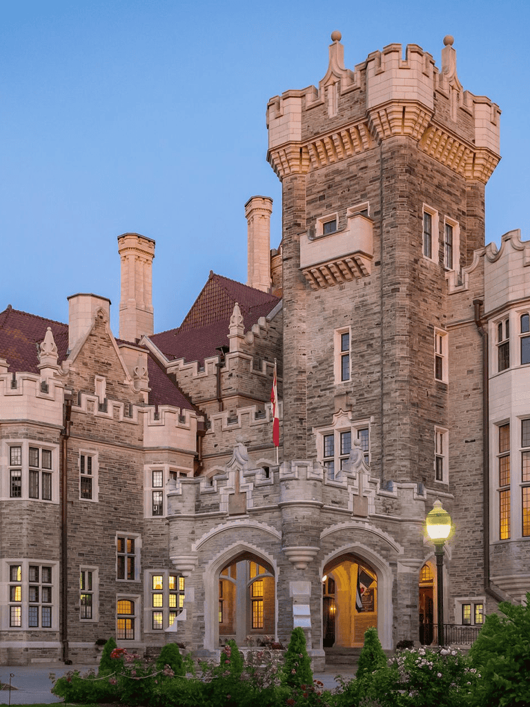 Intricate castle exterior with Gothic architecture, stone walls, turrets, and drawbridge at dusk.