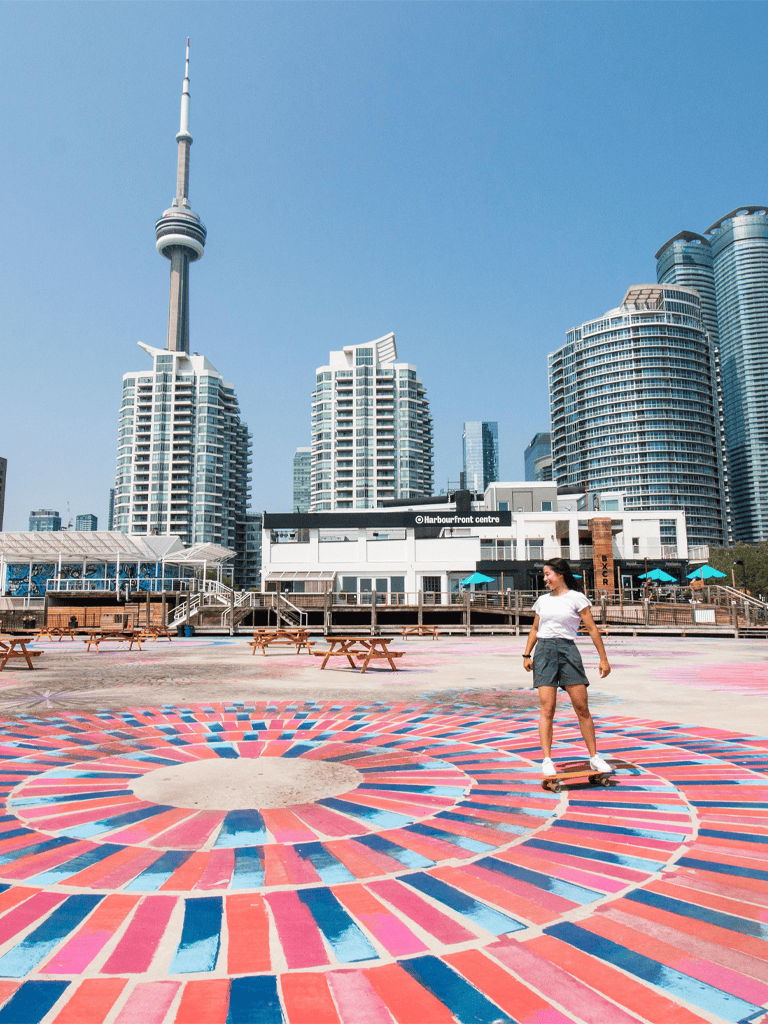 Vibrant urban Toronto waterfront with skateboarding woman and city skyline in background.