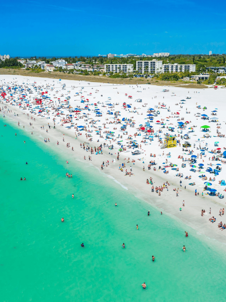 Bright sunny beach with umbrellas, sunbathers, and turquoise ocean waters in Florida.