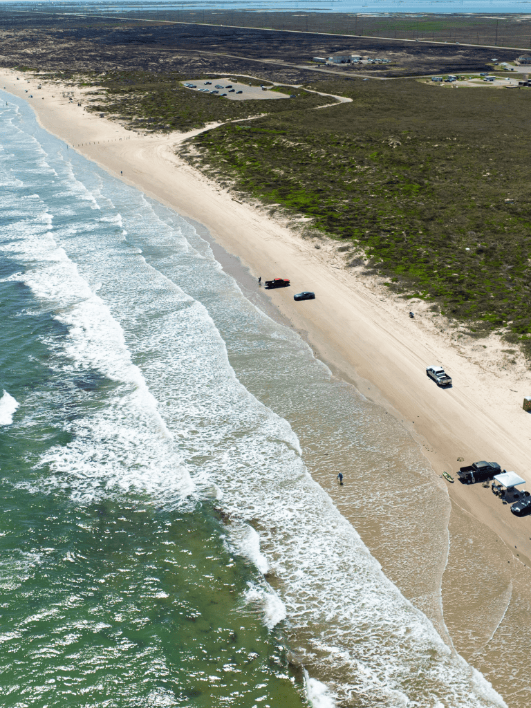 Seaside beach with cars parked on sandy shore and waves crashing, scenic coastal destination.