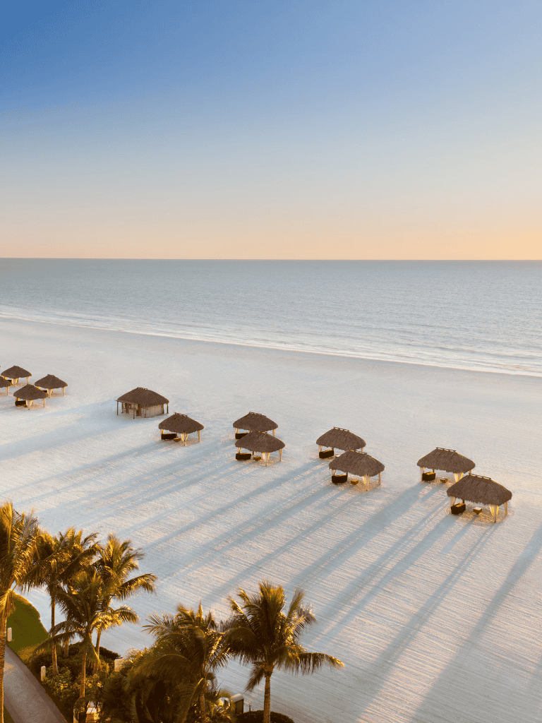 Serene beach with straw huts and palm trees at sunrise or sunset, perfect for relaxing and vacation planning.