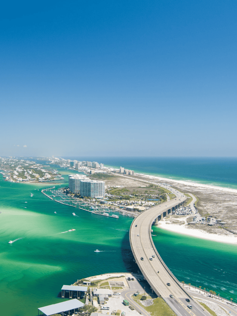 Aerial view of coastal city with bridge, boats, and ocean, showcasing scenic Gulf Coast landscape.
