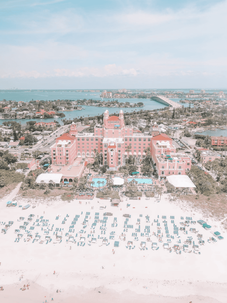 Elegant pink luxury hotel on coastal beach with pools and sun loungers, scenic water views.
