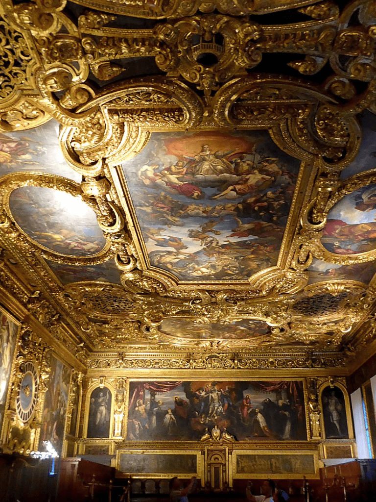 Lavish gold-gilded ceiling with ornate Baroque artwork and grand paintings in an opulent historic interior.