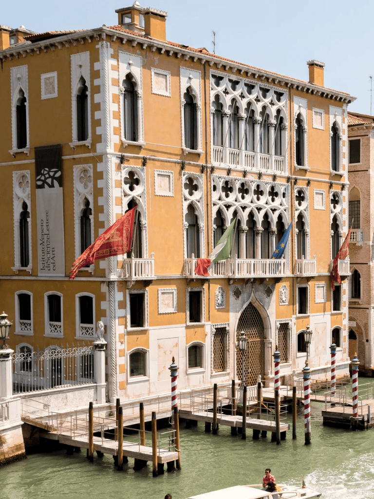 Venetian building in Venice, Italy with canal and gondola, historic Italian architecture, and vibrant flags Seaside Venetian building showcasing classic architecture, canal, gondola, and flags in Venice, Italy.