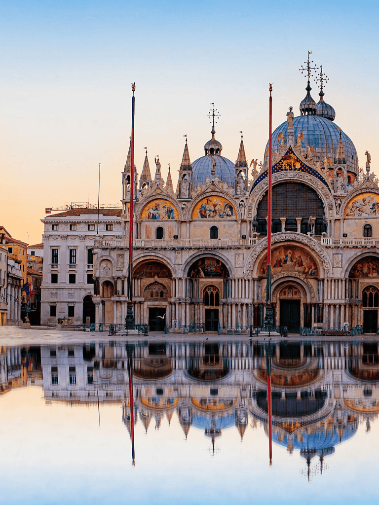 Ancient Venetian church with ornate architecture and reflection in water during sunset.