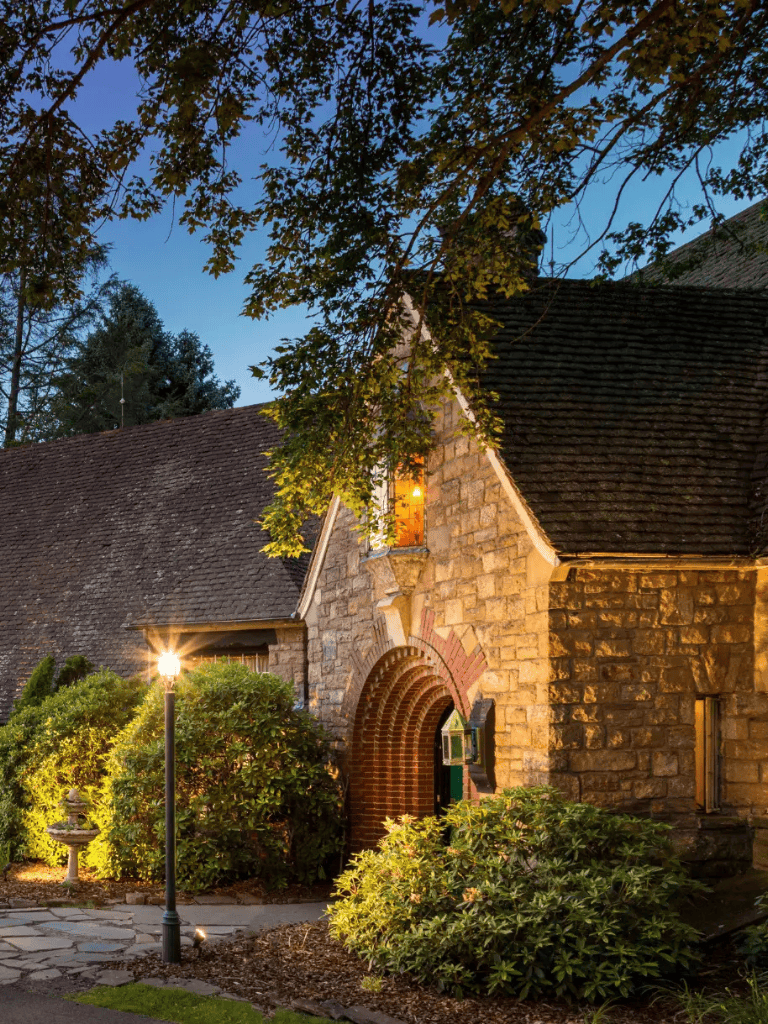 Cozy stone cottage illuminated at dusk with garden and pathway, charming rural retreat.