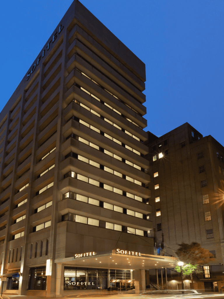 Modern Sofitel hotel building at dusk with illuminated signage and cityscape background.
