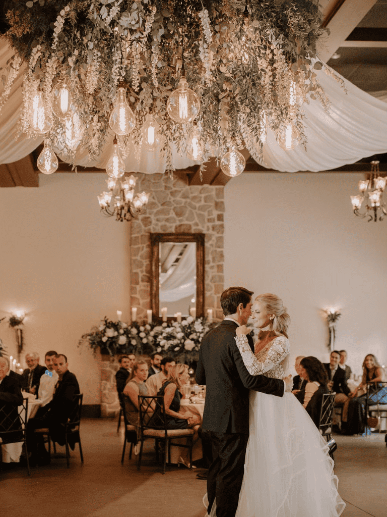 Elegant wedding dance under romantic chandelier lighting with guests in background.