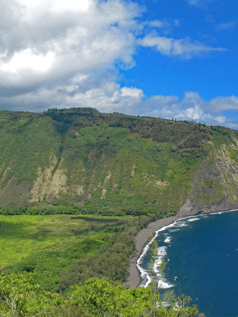 Vast coastal mountain landscape with lush greenery and ocean waves under a partly cloudy sky.