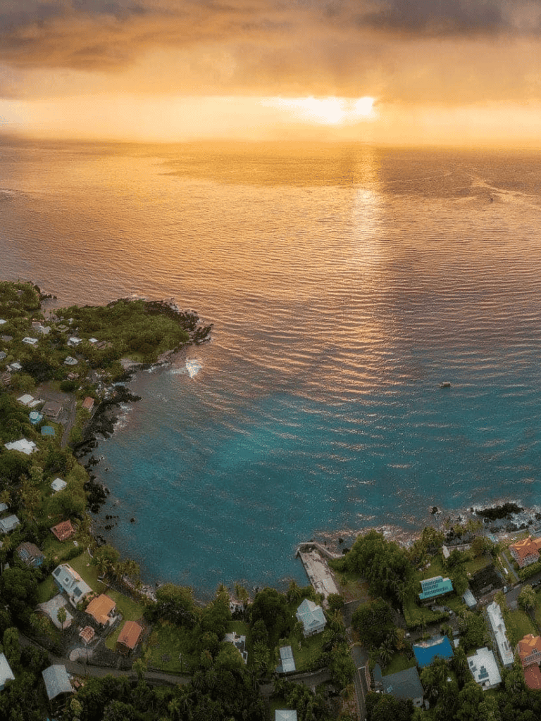 Stunning aerial view of coastal town during sunset, showcasing scenic ocean and lush greenery; perfect for travel and adventure keywords.