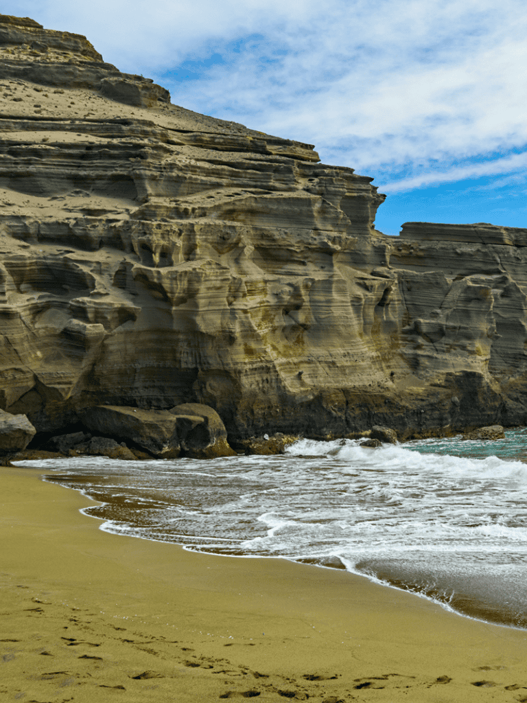 Cliffs and sandy beach along the ocean coastline with blue sky and clouds.