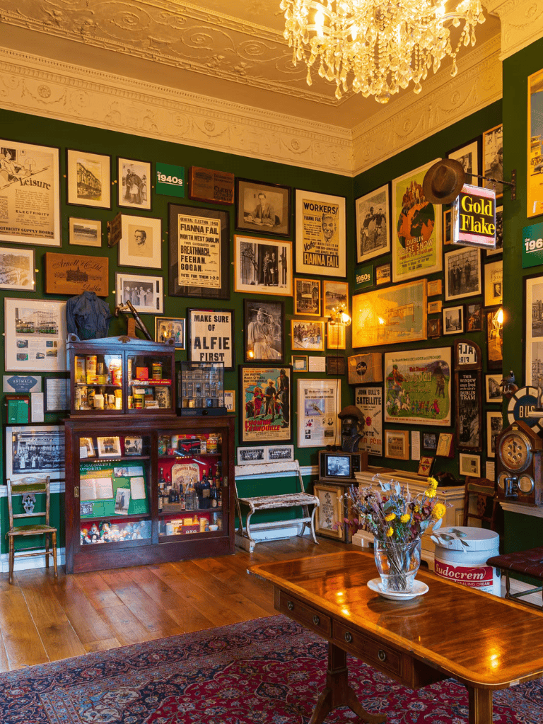 Vintage historical interior with framed posters and memorabilia, cozy atmosphere, wooden furniture, and elegant chandelier.