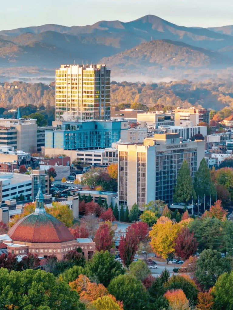 Colorful city skyline with mountains in the background, autumn trees, and modern buildings.