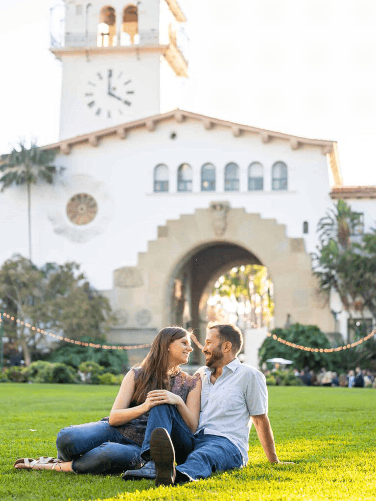 Beautiful couple relaxing on the grassy lawn near a historic clock tower, a perfect spot for romantic dates and city exploration.