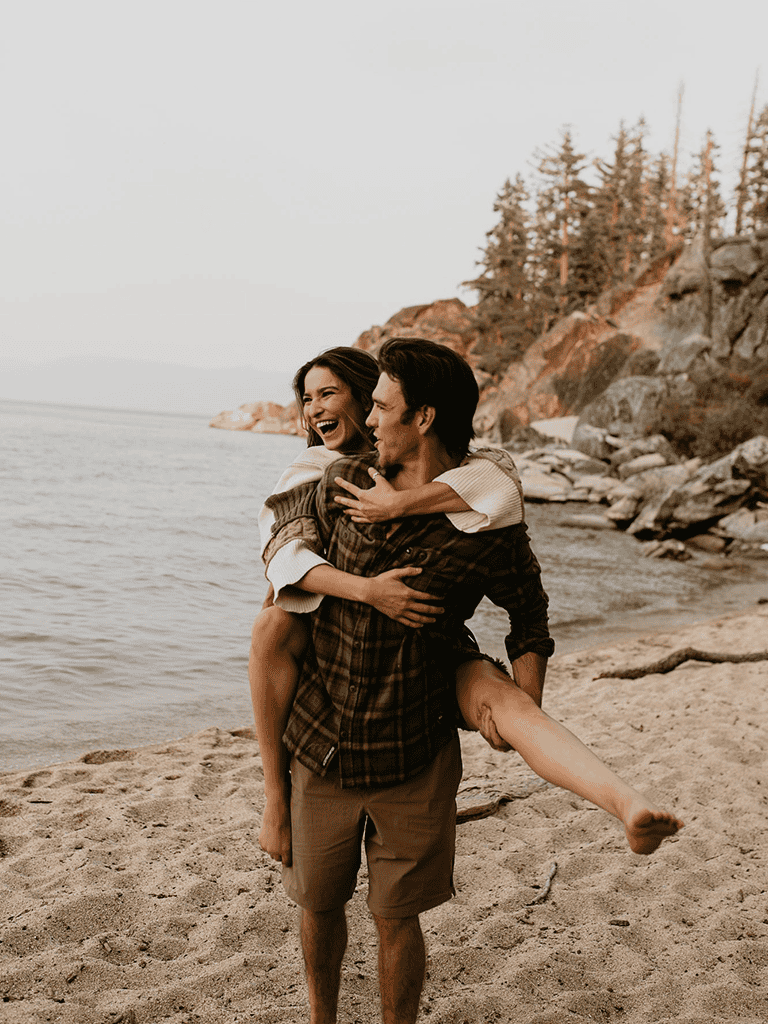 Breathtaking couple on beach enjoying together, scenic coastline and rocky cliffs in background.