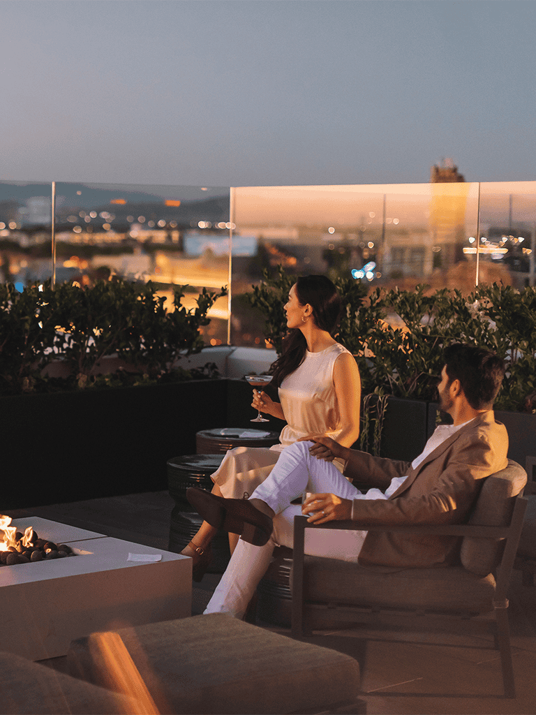 Relaxed couple enjoying rooftop view at QuestForDirections event, evening scenery, city skyline, intimate atmosphere.
