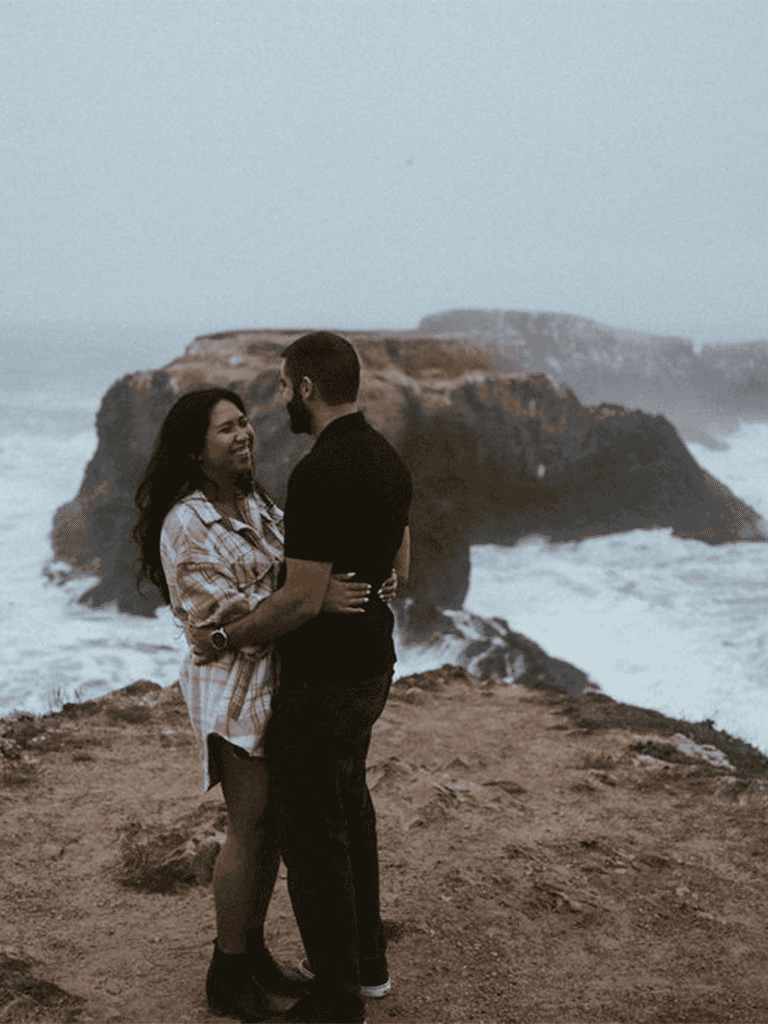 Romantic couple embracing at coastal cliffs during sunset, scenic ocean background, travel and adventure romance.
