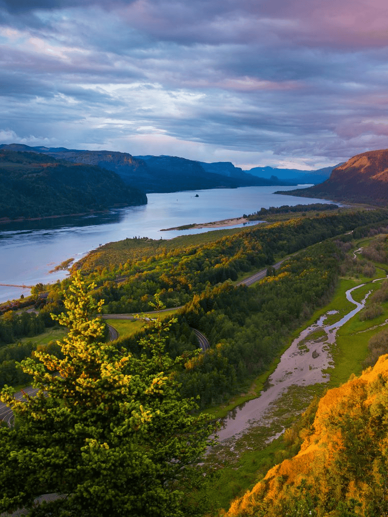 Breathtaking river valley scenery with lush green forests and mountain views during sunset.