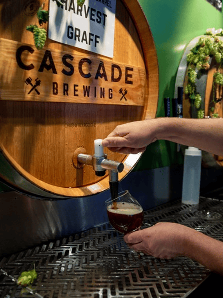Craft beer being poured from a keg at Cascade Brewing, with Harvest Graff sign in the background.
