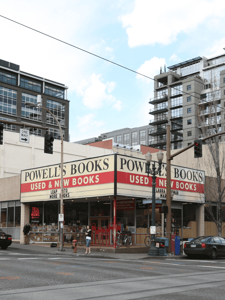 Used bookstore storefront with Powell's Books signage, cityscape background, and pedestrians in Portland, Oregon.