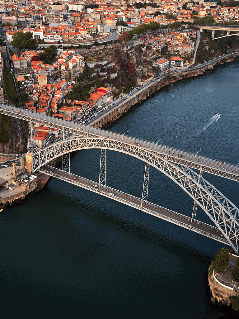 Suspension bridge over water connecting hilly cityscape with colorful buildings.